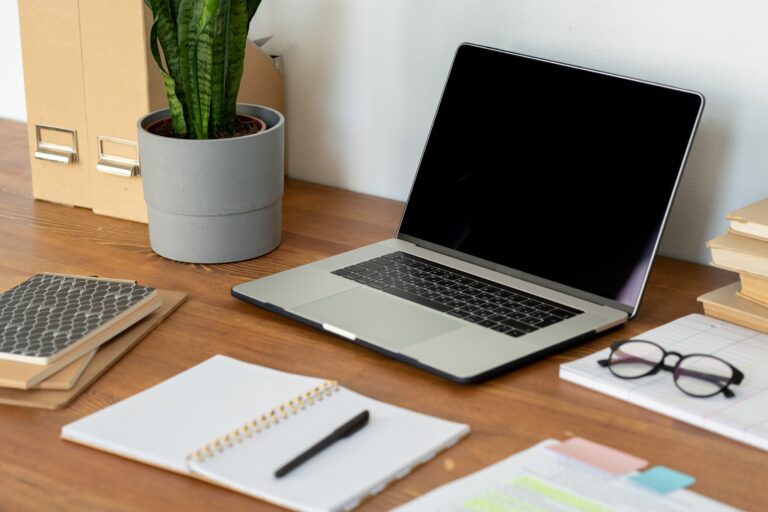 Workplace of home office employee with laptop, eyeglasses, open notebook with pen and other supplies on wooden table